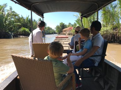 Eine Gruppe von Kindern und Erwachsenen genießt eine Bootstour durch den Mekong-Delta, umgeben von üppigem Grün.