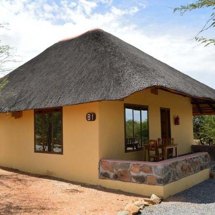 Ein gemütliches, strohgedecktes Häuschen mit großen Fenstern, umgeben von trockenem, buschigem Gelände.