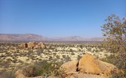 Eine weite Landschaft mit großen Felsen und sanften Hügeln unter einem klaren blauen Himmel, der die Ruhe der Natur widerspiegelt.