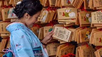 Eine Frau in einem Kimono betrachtet sorgfältig hölzerne Tafeln mit Wünschen und Zeichnungen in einem Tempel in Kyoto.