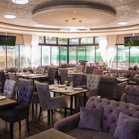 Elegante Restaurant mit stilvollen, gepolsterten Stühlen und Tischen, umgeben von großen Fenstern und sanften Vorhängen.