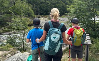 Eine Frau steht mit zwei Kindern am Wanderweg und blickt auf die beeindruckenden Berge im Hintergrund.