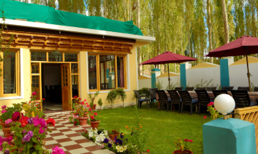 Ein einladendes Hotel mit bunten Blumenbeeten und einem gepflegten Garten, umgeben von hohen Bäumen und Sonnenschirmen.