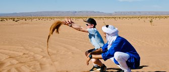 Guide und Kind spielen gemeinsam und werfen Sand in der weiten Wüste – Familienreise nach Marokko