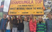 Eine Gruppe von sieben Jugendlichen posiert fröhlich vor dem Schild am Khardungla Pass, dem höchsten befahrbaren Weg der Welt.