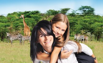 Eine Frau trägt ein Mädchen auf dem Rücken, während im Hintergrund Giraffen und Zebras in einer grünen Landschaft zu sehen sind.