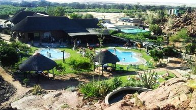 Eine weitläufige Anlage mit mehreren Schwimmbecken, umgeben von grüner Vegetation und Felsen im Hintergrund.