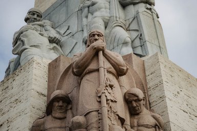 Ein monumentales Denkmal mit einer beeindruckenden Statue eines Kriegers, der einen Stock hält, umgeben von weiteren Figuren.