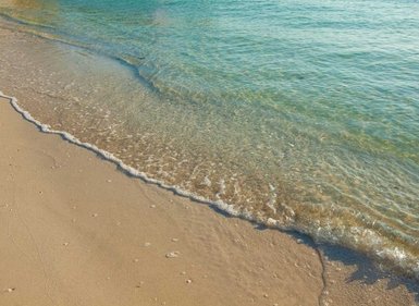 Sanfter Wellenlauf trifft auf den feinen Sandstrand, während das klare Wasser in der Sonne glitzert.