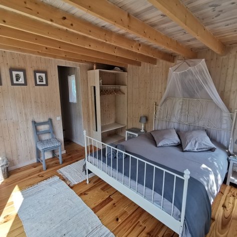 Ein gemütliches Schlafzimmer mit einem weißen Bett, grauer Bettwäsche und Holzdecke, das eine entspannende Atmosphäre ausstrahlt.