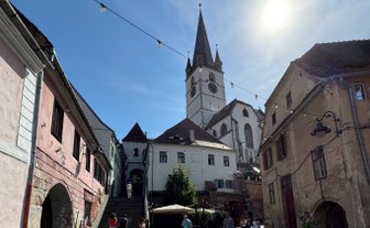 Eine belebte Straße in Sibiu mit historischen Gebäuden und einer markanten Kirche im Hintergrund unter klarem Himmel.