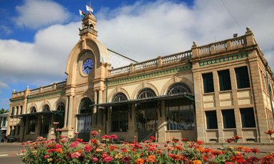 Die beeindruckende Fassade des Bahnhofs in Antananarivo, umgeben von bunten Blumen und unter einem strahlend blauen Himmel.