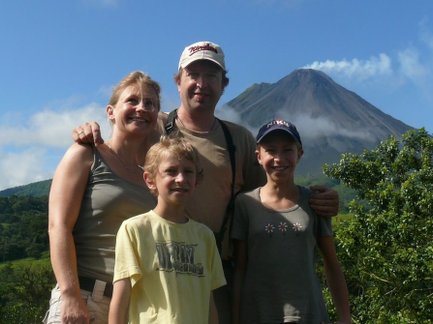 Eine Familie posiert fröhlich vor einem majestätischen Vulkan in Costa Rica, umgeben von üppiger Natur und klarem Himmel.