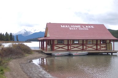 Ein rotes Bootshaus am Ufer des Maligne Lake, umgeben von Bergen und Bäumen, spiegelt sich im ruhigen Wasser wider.