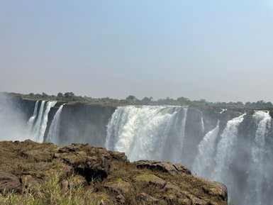Majestätische Wasserfälle stürzen über eine Klippe, umgeben von üppigem Grün und einem klaren blauen Himmel.