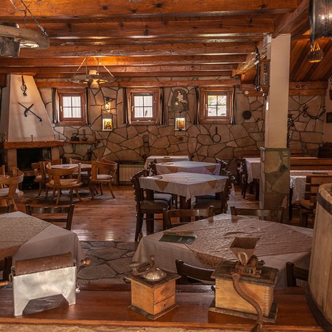 Ein rustikales Restaurant mit Holzmöbeln, Tischen und einer gemütlichen Atmosphäre, beleuchtet von warmem Licht.