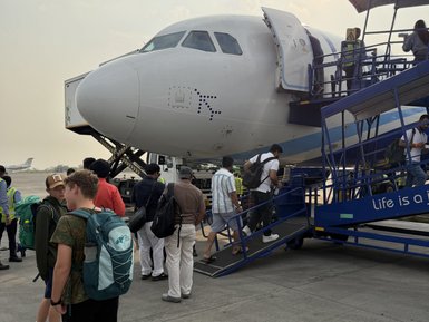 Eine Gruppe von Passagieren steigt an einem Flughafen in ein Flugzeug ein, während die Sonne am Horizont untergeht.