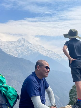 Ein Junge mit einem Hut steht nachdenklich auf einem Felsen und blickt auf die majestätischen schneebedeckten Berge.