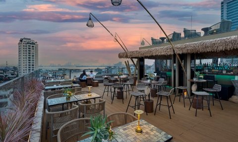 Eine stilvolle Dachterrasse mit modernen Möbeln, umgeben von Pflanzen und einem atemberaubenden Sonnenuntergang über der Stadt.