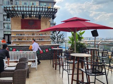 Eine stilvolle Dachterrasse mit einer Bar, umgeben von Pflanzen und einem Blick auf die Stadt, während ein Kellner vorbeigeht.