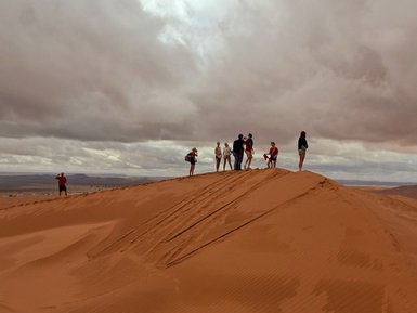 Eine Gruppe von Jugendlichen steht auf einer Sanddüne, umgeben von bewölktem Himmel und einer weiten Wüstenlandschaft.