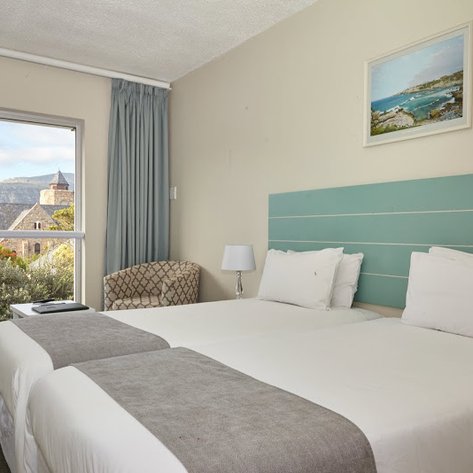 Ein helles Zimmer mit zwei Einzelbetten, einem gemütlichen Sessel und einem Fenster, das auf eine malerische Landschaft blickt.