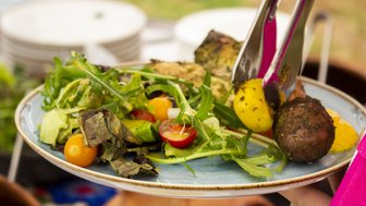 Ein Teller mit frischem Salat, bunten Tomaten und einer gelben Kartoffel wird mit einer Zange serviert.
