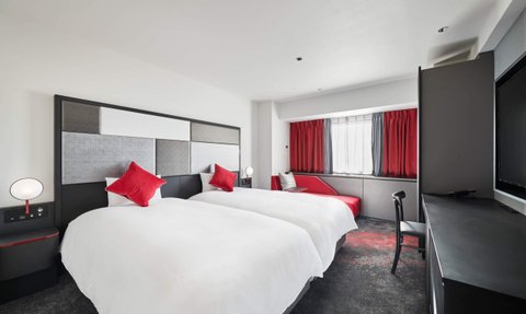 Zwei Einzelbetten mit roten Kissen in einem modernen Hotelzimmer, das hell und einladend wirkt.