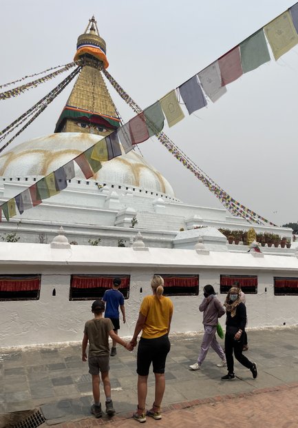 Eine Familie mit zwei Kindern erkundet den Bodhnath Stupa, umgeben von bunten Gebetsfahnen und einer spirituellen Atmosphäre.
