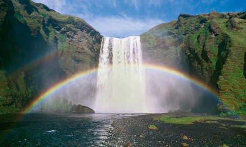 Ein majestätischer Wasserfall stürzt in einen klaren Fluss, während ein strahlender Regenbogen die Szenerie überquert.