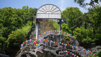 Eine bunte Treppe aus Ballons führt zu einer beeindruckenden Felsformation, die von üppigem Grün umgeben ist.