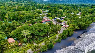 Eine üppige grüne Landschaft mit Bungalows und Straßen, die sich an der Küste entlangschlängeln, vermittelt tropisches Flair.
