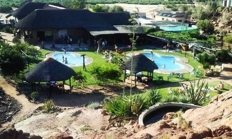 Eine weitläufige Anlage mit mehreren Schwimmbecken, umgeben von grüner Vegetation und Felsen im Hintergrund.