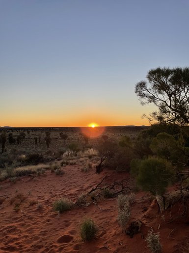 Ein atemberaubender Sonnenuntergang über der roten Wüstenlandschaft, beleuchtet durch sanfte orangefarbene Töne.
