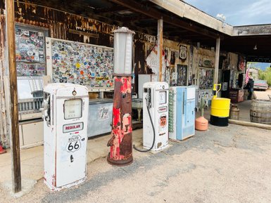 Eine alte Tankstelle mit mehreren Vintage-Tankstellen und einer Wand voller Aufkleber, die Erinnerungen an Route 66 wecken.
