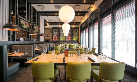 Ein modernes Restaurant mit grünen Stühlen und eleganten Tischen, beleuchtet von großen, runden Lampen.