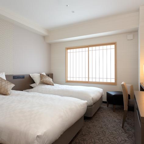 Ein modernes Hotelzimmer mit zwei Einzelbetten, eleganten Kissen und einem großen Fenster, das viel Tageslicht hereinlässt.