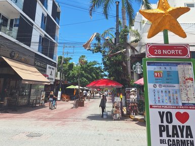 Eine belebte Straße in Playa del Carmen mit bunten Schirmen und einem großen, goldenen Stern auf einem Schild.