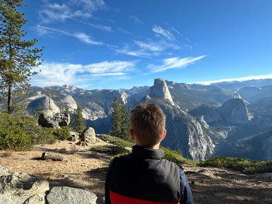 Ein junger Mann sitzt auf einem Felsen und blickt auf die majestätischen Berge des Yosemite Nationalparks.
