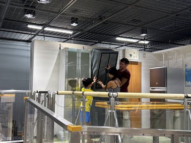 Eine Frau und ein Mann helfen einem Kind, einen großen Schrank während einer Erdbebensimulation zu stabilisieren.