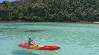 Erwachsener fährt in Kanu über kristallklares Wasser auf Inselparadies Koh Talu - Thailand mit Kindern