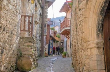 Eine enge Gasse mit steinernen Wänden, gesäumt von traditionellen Häusern und einem blühenden Topf auf dem Boden.