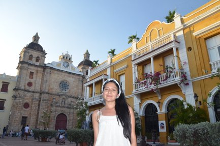 Eine Frau mit langen, schwarzen Haaren steht vor der Kirche San Pedro Claver, umgeben von bunten Gebäuden in Cartagena.