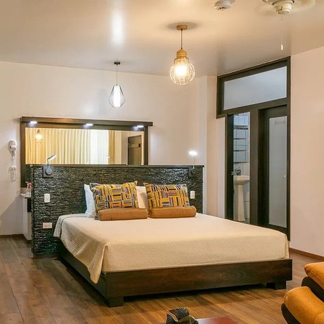 Ein modernes Hotelzimmer mit einem großen Bett, bunten Kissen und warmem Holzfußboden, das Gemütlichkeit ausstrahlt.