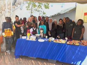 Eine fröhliche Gruppe von Menschen versammelt sich um einen Tisch mit Essen und Getränken, umgeben von einer einladenden Atmosphäre.