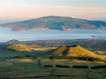 Eine atemberaubende Aussicht auf die grüne Landschaft und den Ozean, mit sanften Hügeln und einem majestätischen Berg im Hintergrund.