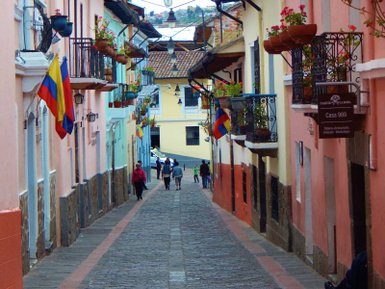 Eine malerische Gasse mit bunten Häusern und Blumen, in der Menschen entspannt spazieren gehen.