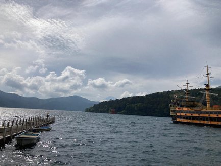 Ein Piratenschiff fährt auf dem ruhigen Wasser des Ashi-Sees, umgeben von grünen Bergen und dramatischen Wolken.