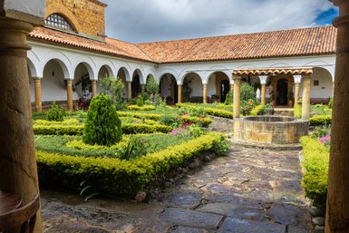 Ein malerischer Innenhof mit bunten Blumenbeeten und einem zentralen Brunnen, umgeben von historischen Säulen und Bögen.