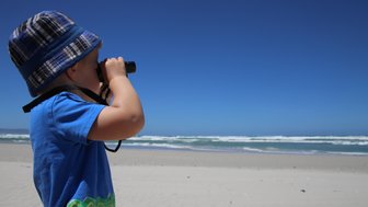 Ein Kind beobachtet aufmerksam das Meer mit Ferngläsern am Grotto Beach in Hermanus – Südafrika mit Kindern